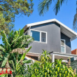 After - Bronte A modern two-story house with dark gray siding and large windows, surrounded by lush green tropical plants and trees under a clear blue sky. The 32 Degrees Building logo is in the bottom left corner.